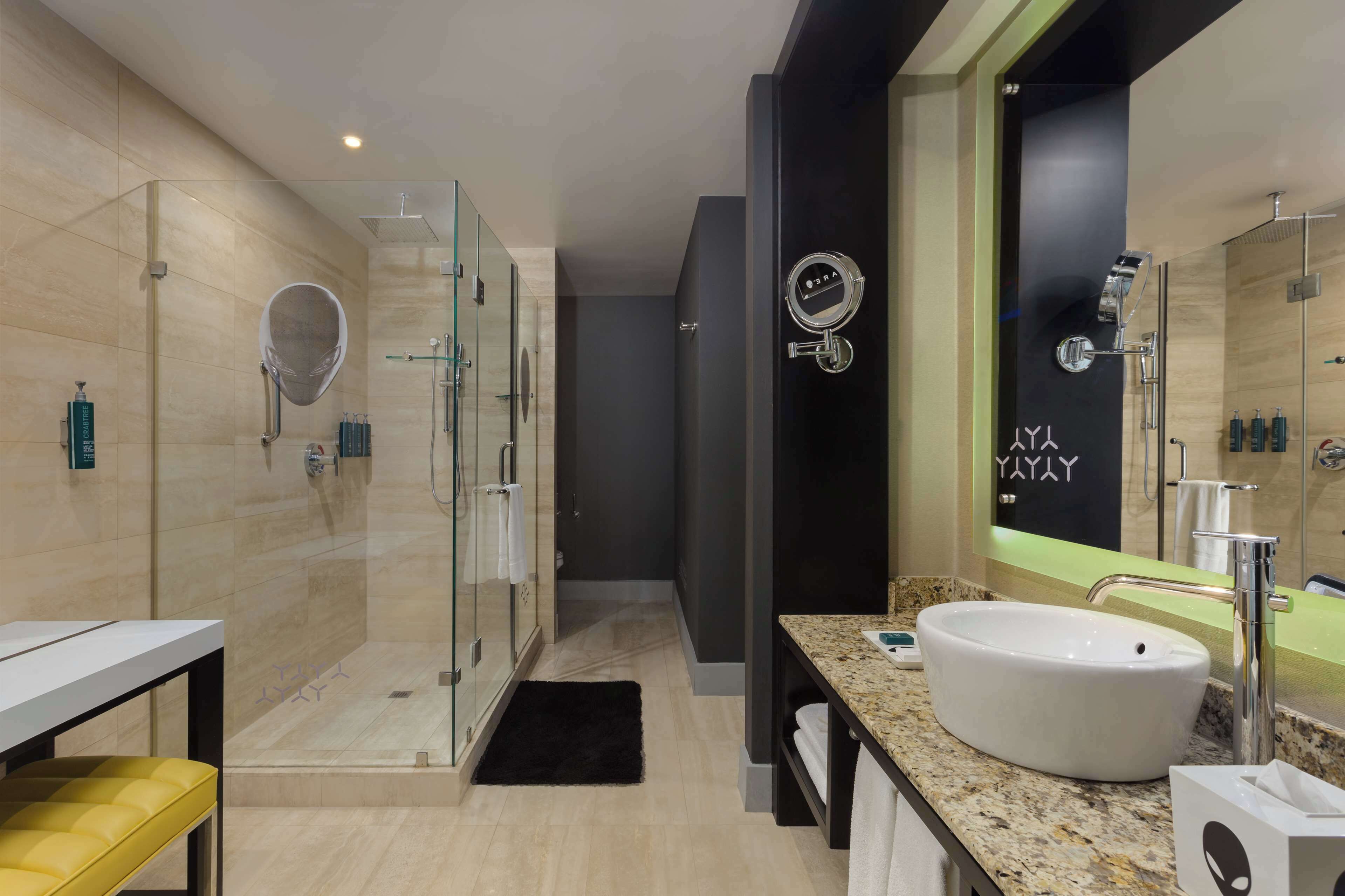 Un baño moderno con ducha de vidrio, un espejo grande y lavamanos sobre encimera de granito.