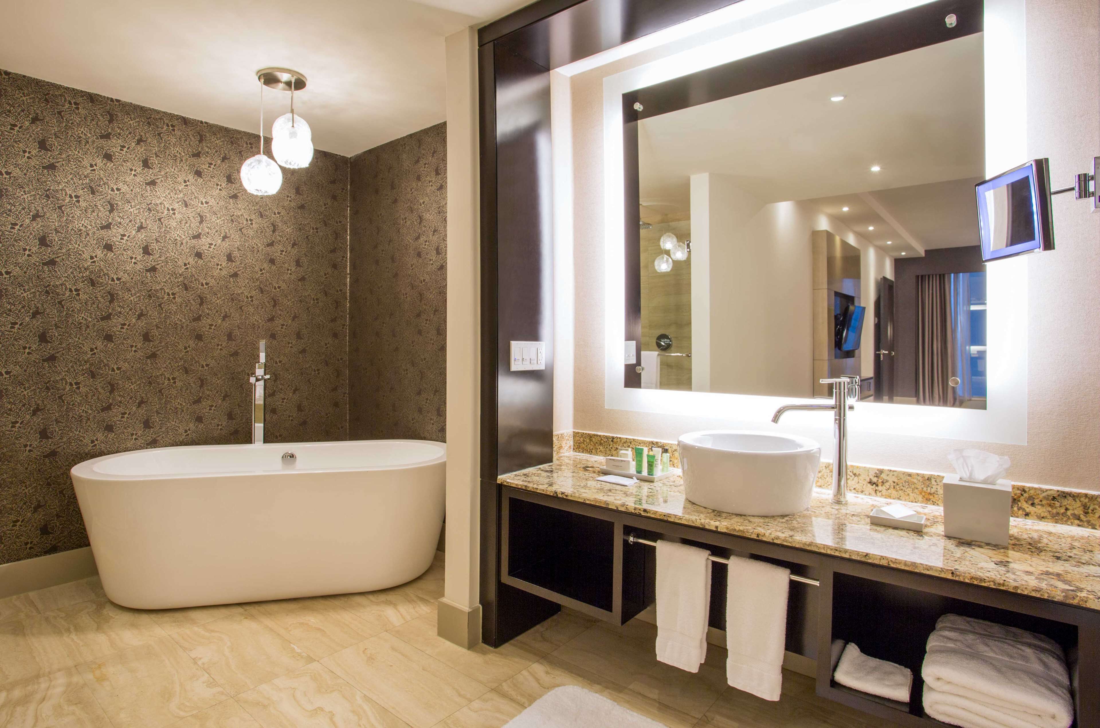 Un baño moderno con una bañera independiente, un espejo grande y una encimera de granito.