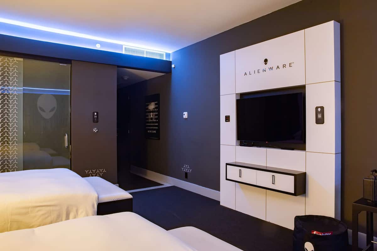 A modern hotel room with a large flat-screen TV, a minibar, and a wardrobe.