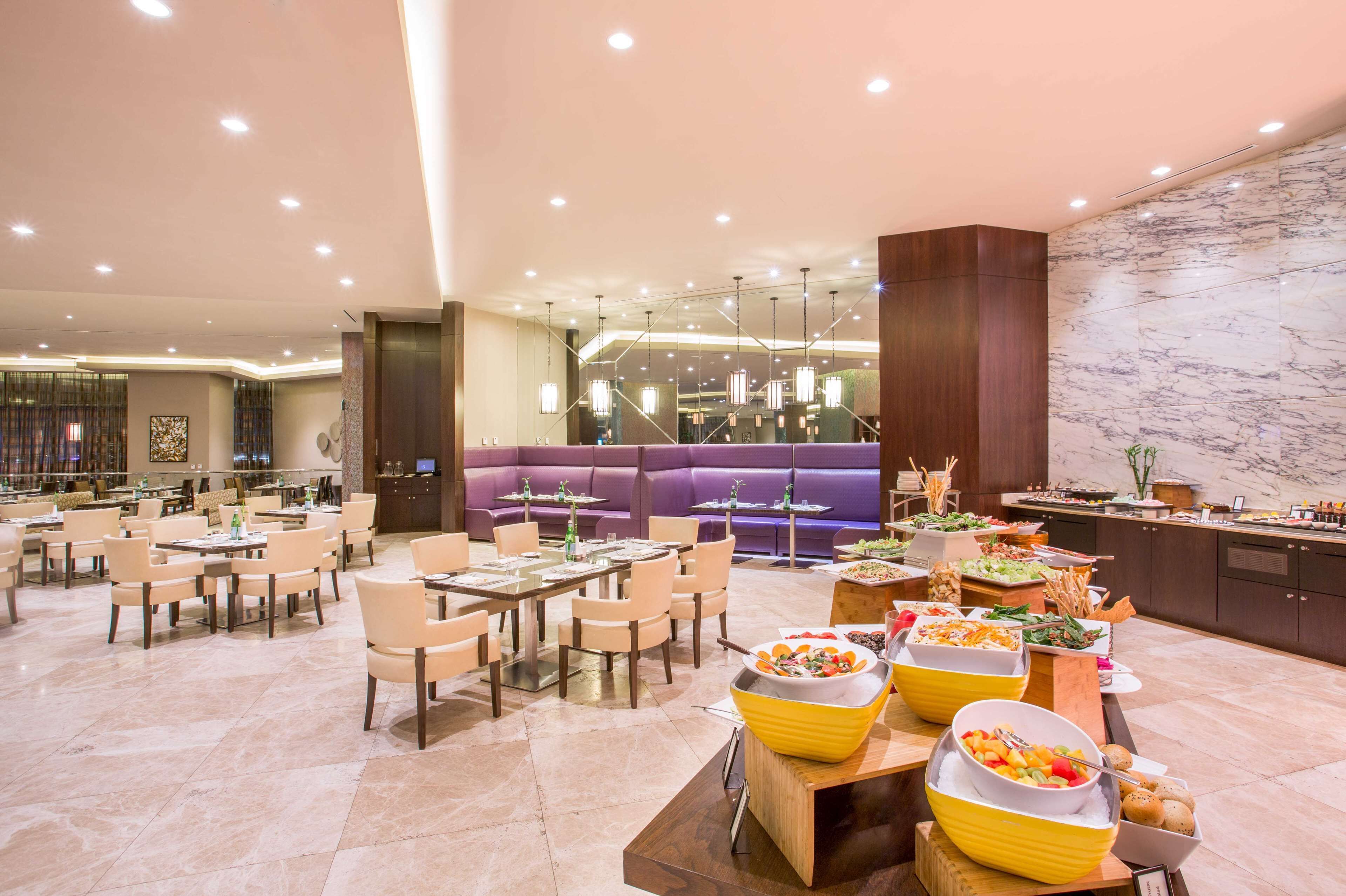 Un amplio vestíbulo de hotel con varias zonas de estar, un bufé con diferentes opciones de comida y una pared de mármol.