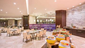 Un amplio vestíbulo de hotel con varias zonas de estar, un bufé con diferentes opciones de comida y una pared de mármol.