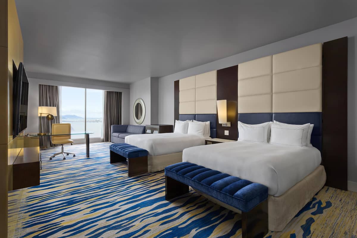 A hotel room with two beds, a sofa, a desk, and a large window.