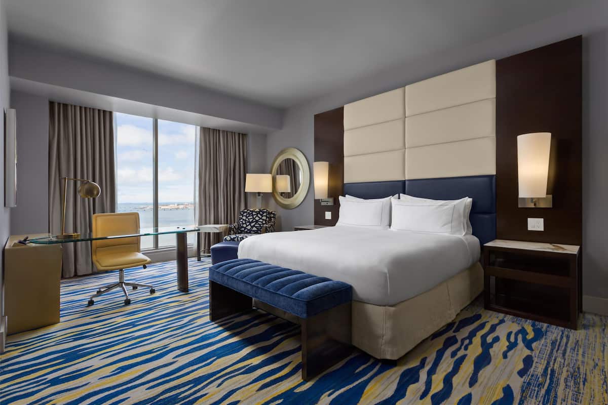 A hotel room with a large bed, a desk, a chair, and a view of the city.