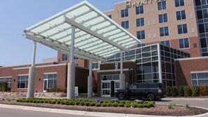 A modern hotel entrance with a covered walkway, a black SUV parked in front, and a clear sky. - Hyatt Place Detroit/Novi (Novi)