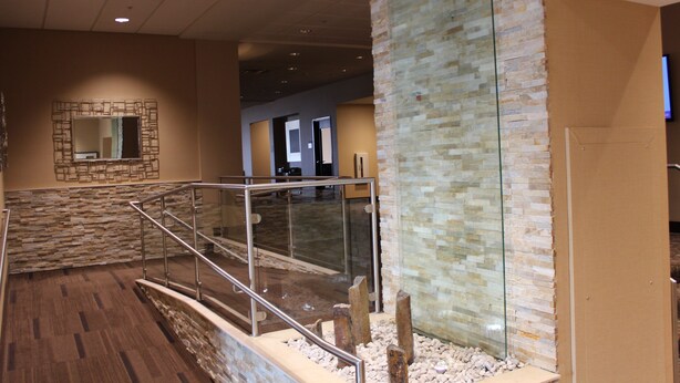 A modern lobby with a stone wall, a glass water feature, and a wooden floor. - Hyatt Place Detroit/Novi (Novi)