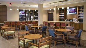 A restaurant with multiple tables and chairs, a bar area with shelves of bottles, and a television screen displaying a warning message. - Hyatt Place Detroit/Novi (Novi)