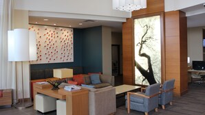 A modern hotel lobby with a seating area, a large wall art piece, and a desk with a computer.