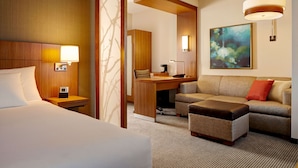 A hotel room with a bed, a desk, a sofa, and a painting on the wall. - Hyatt Place Detroit/Novi (Novi)