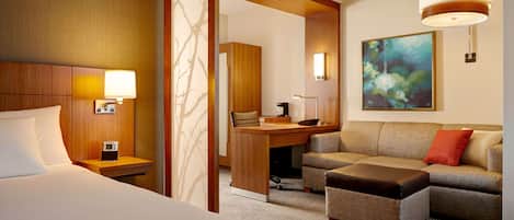 A hotel room with a bed, a desk, a sofa, and a painting on the wall.