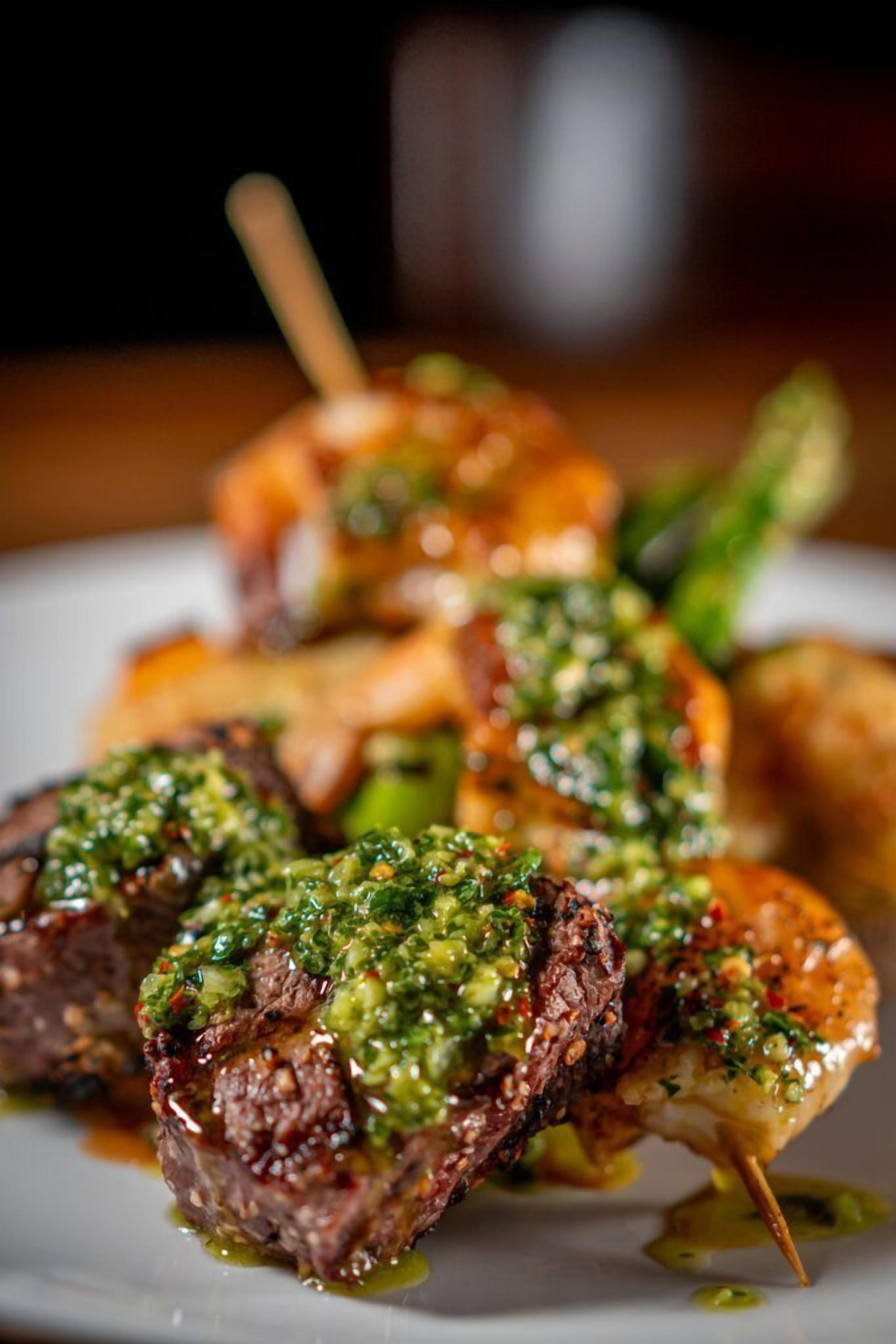 A plate with skewered meat and vegetables, garnished with a green sauce.