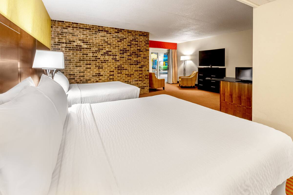 A hotel room with two beds, a brick wall, a TV, and a desk.