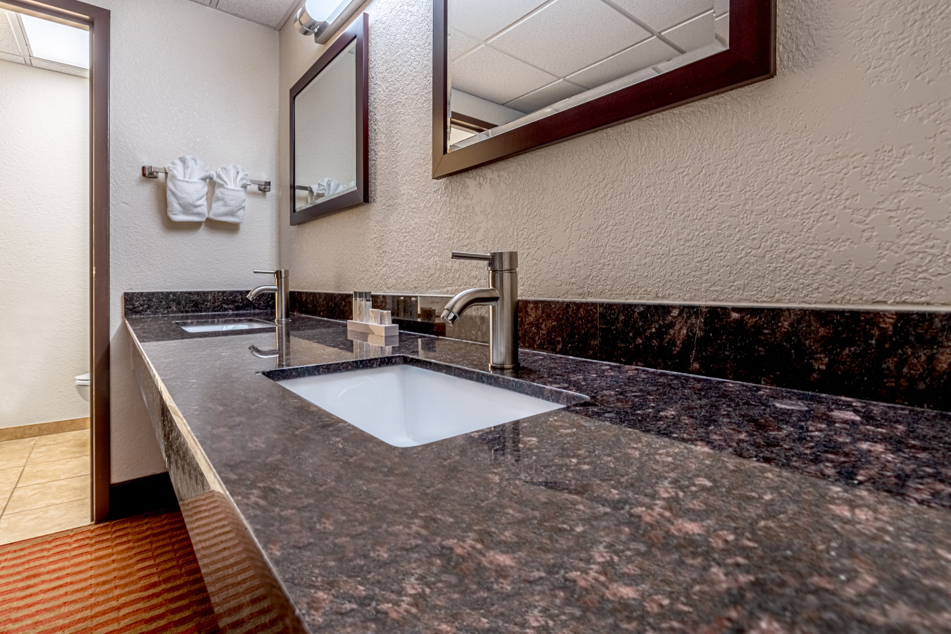 Un baño moderno con encimera de granito, dos lavabos y un espejo grande.