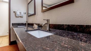 Un baño moderno con encimera de granito, dos lavabos y un espejo grande.