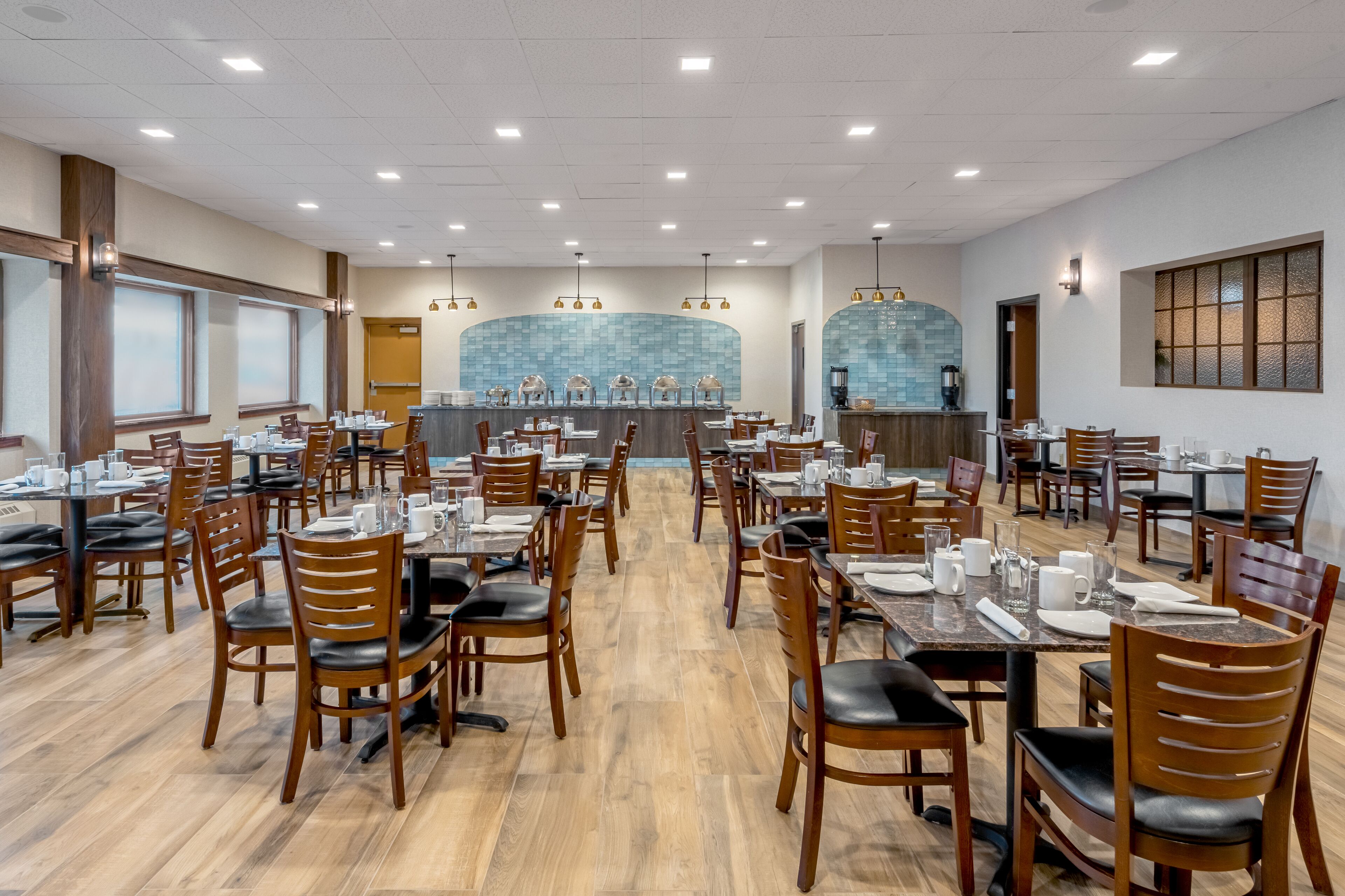 Un vaste espace dédié à la salle à manger, avec de nombreuses tables et chaises, un bar central et une vue sur la cuisine grâce à une paroi en verre.