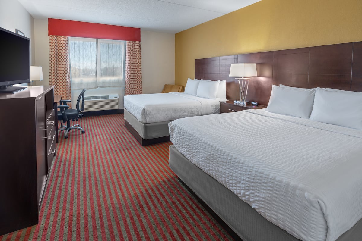 A hotel room with two beds, a desk, a TV, and a window with curtains.