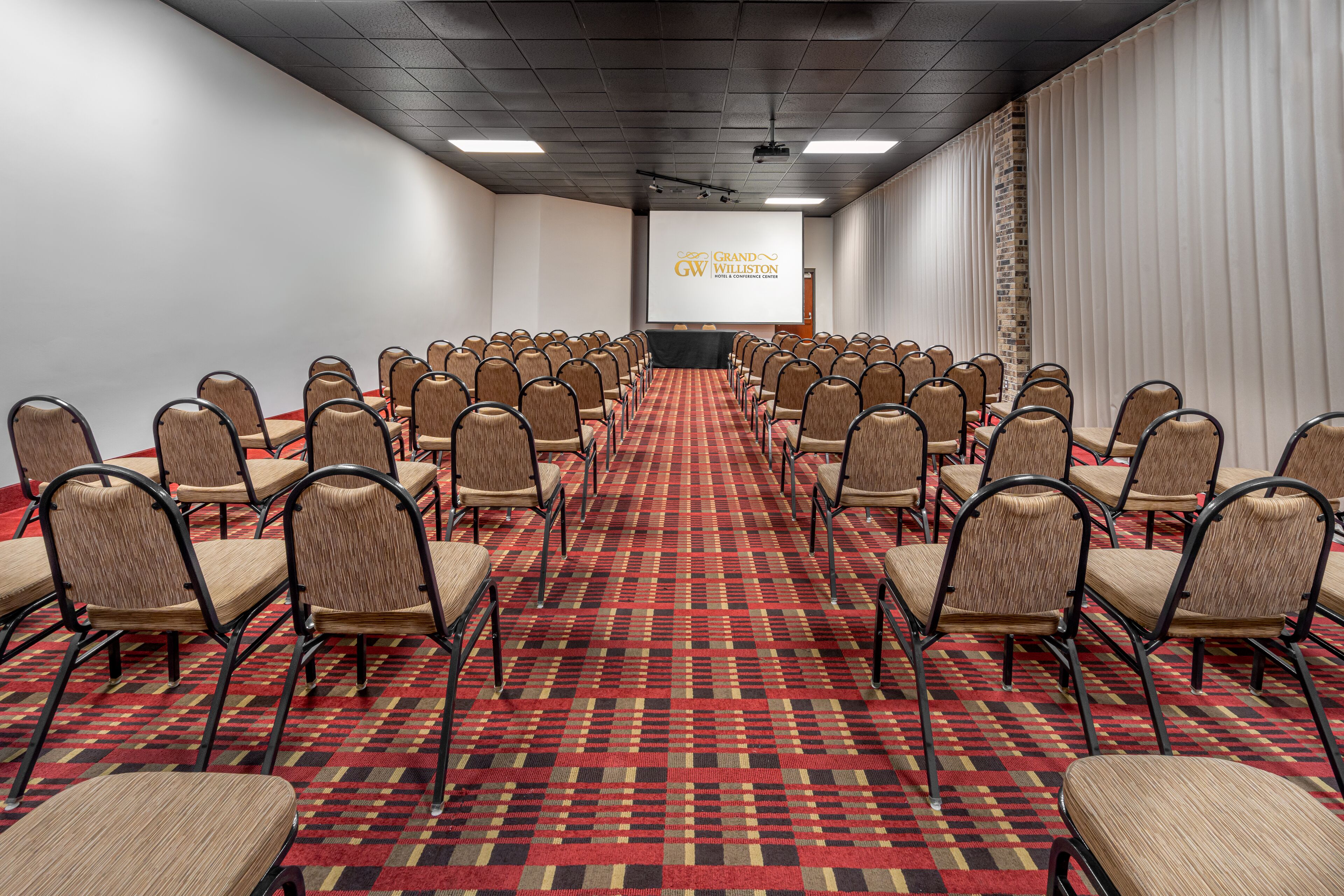 A conference room with rows of chairs, a red patterned carpet, and a projection screen displaying "Grand Williston".