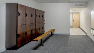 Un couloir avec des casiers, un banc et une porte au fond.