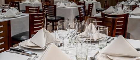 Un restaurante con varias mesas dispuestas para comer, cada una con manteles blancos, cubertería y cristalería.