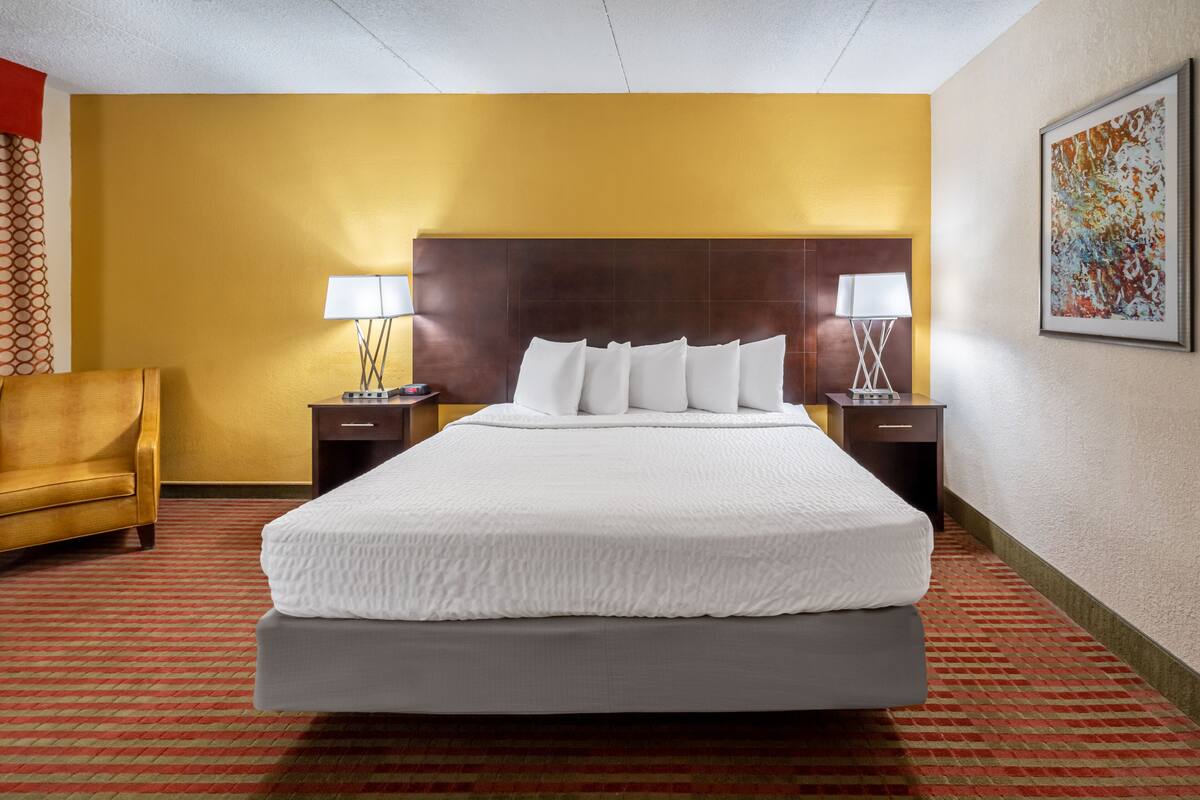 A hotel room with a large bed, two bedside tables with lamps, a chair, and a painting on the wall.