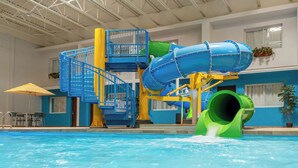 Uma piscina interna com um toboágua, uma escada azul e amarela, e um escorregador verde.
