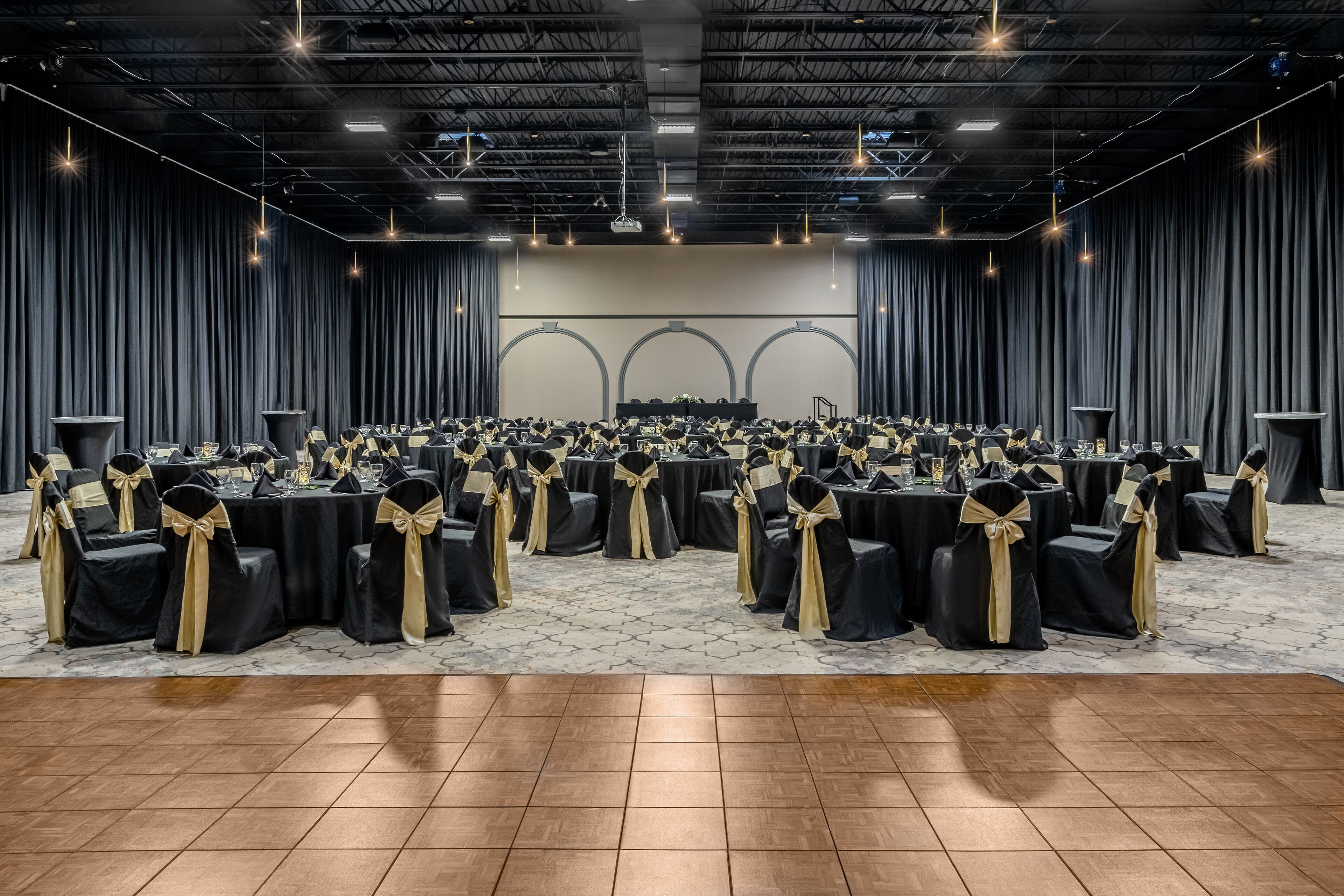 A large conference room with rows of tables and chairs, a stage with a podium, and a high ceiling with industrial lighting.