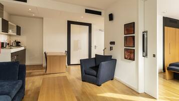 A modern hotel room with a sofa, a small table, a bed, and a kitchenette.