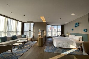 A modern hotel room with a large bed, a sofa, a small table, and a chair. There are large windows with curtains, a ceiling light, and wall-mounted decor. - HanTing Hotel (Shenzhen Huaqiangbei Yannan Subway Station) (Shenzhen)