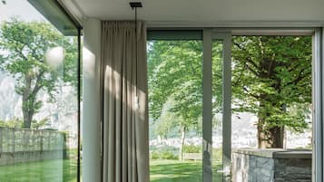 A modern room with a large sliding glass door leading to a garden. Inside, there is a round wooden table with two black chairs.