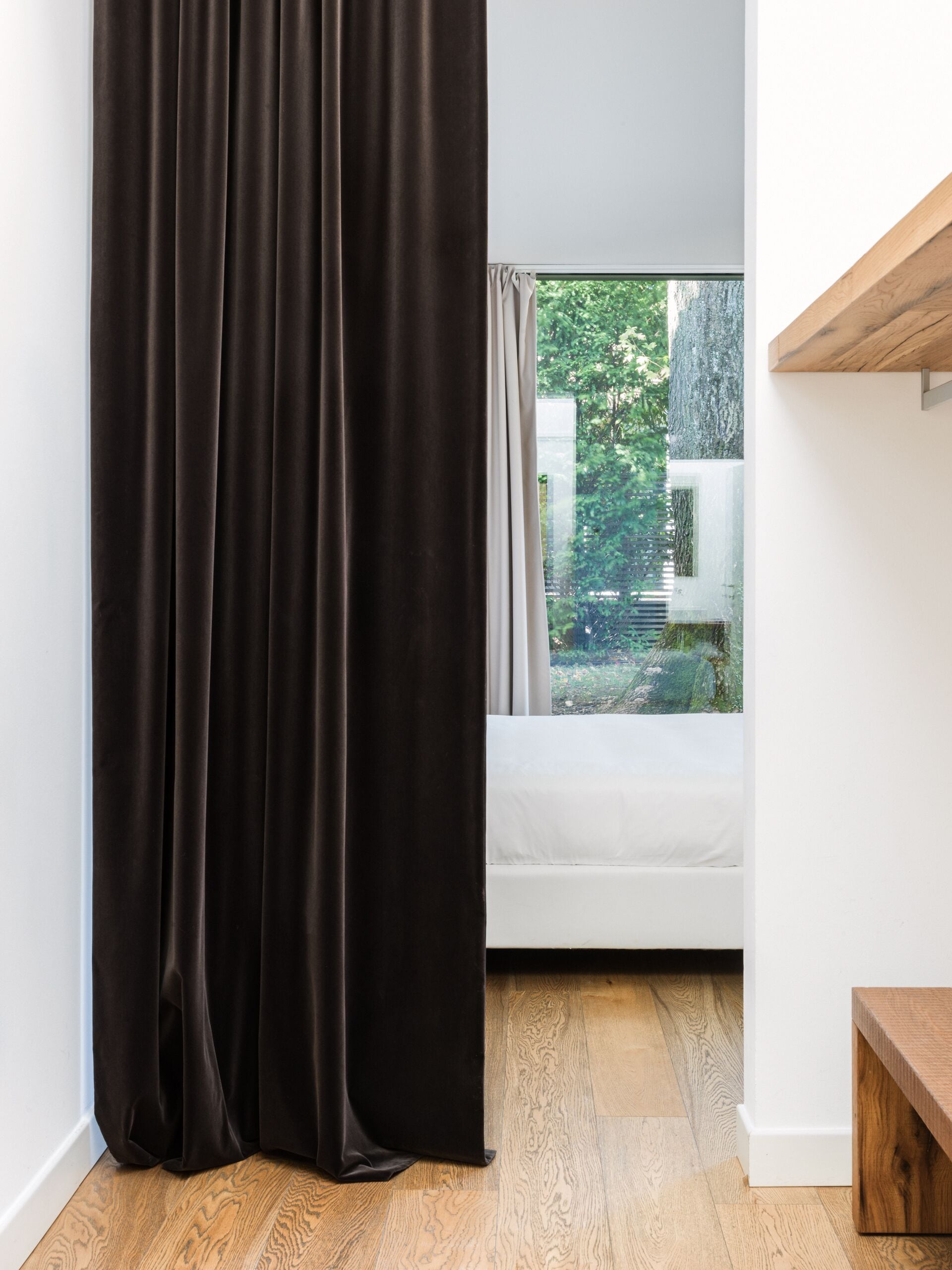 Una stanza con un'ampia finestra, una panca di legno e un letto bianco.