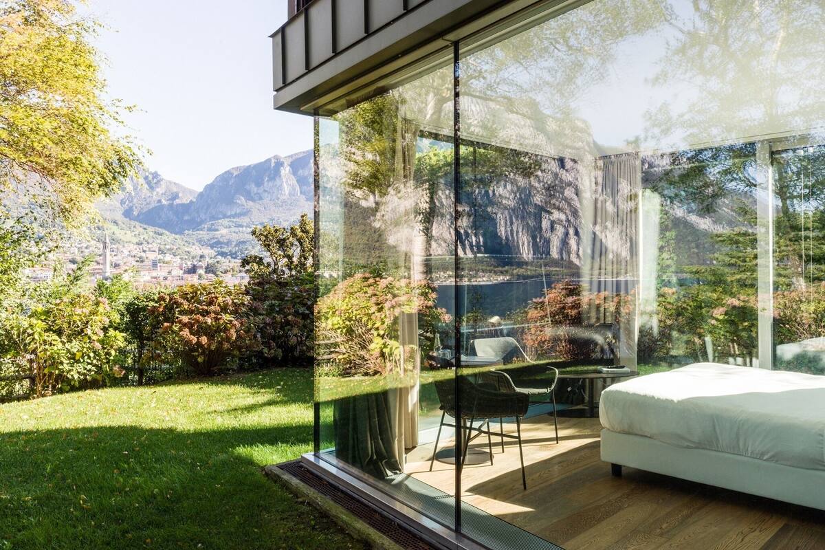 Une chambre moderne avec un mur en verre, un lit et une chaise, donnant sur un paysage montagneux.