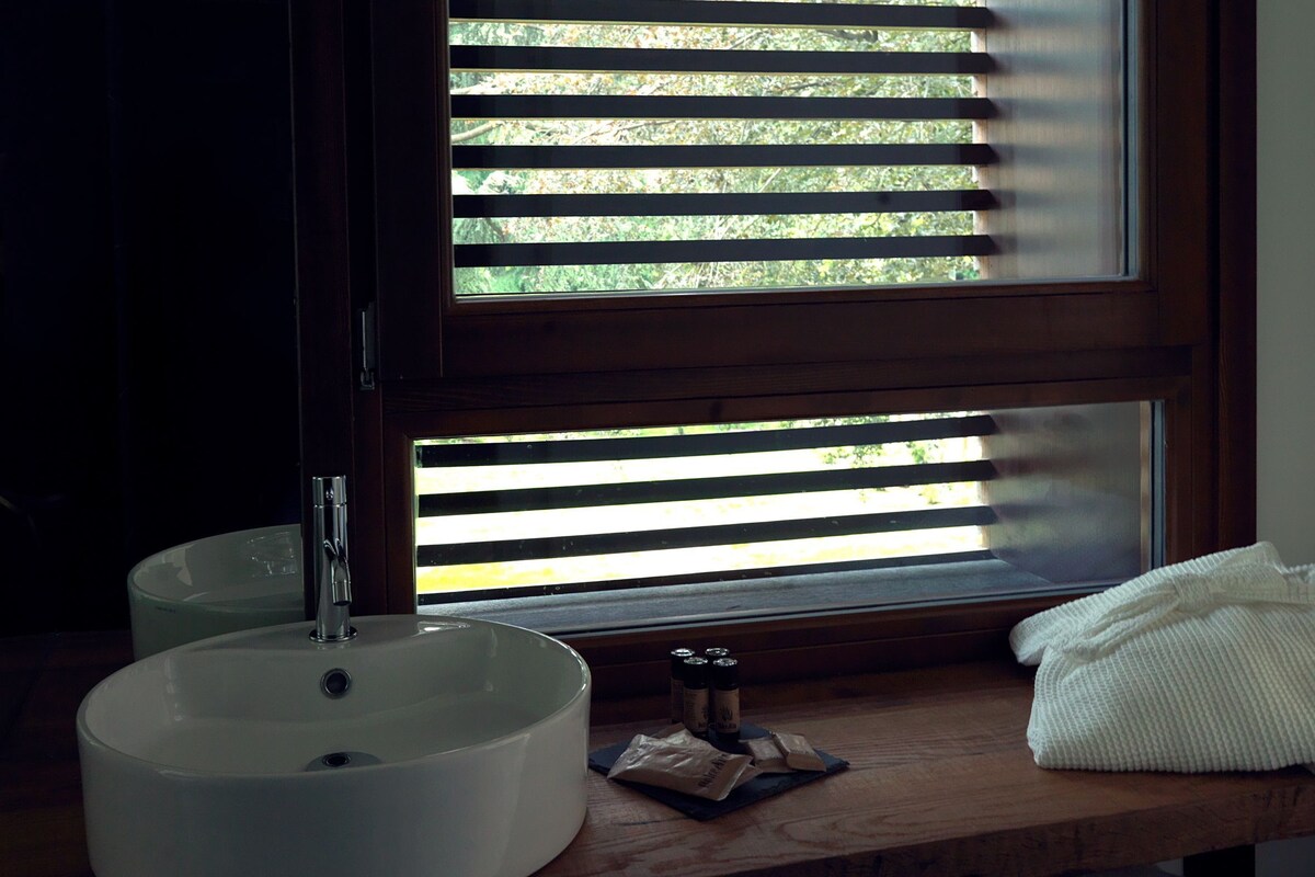 A bathroom with a round sink, a mirror, and a window with blinds.