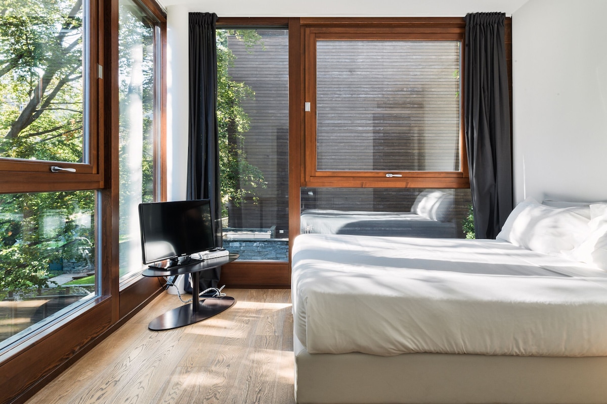 A bedroom with a bed, a TV, and large windows.