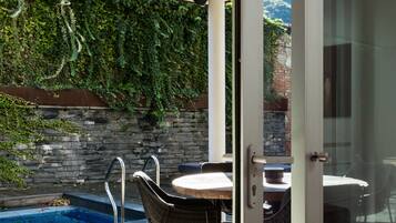 A wooden deck with a pool, outdoor seating, and a stone wall covered in greenery.