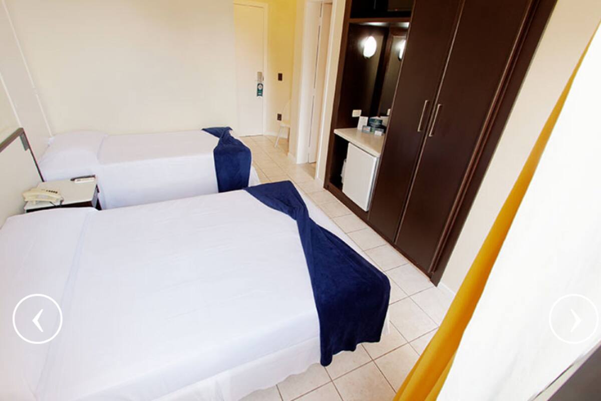 Una habitación de hotel con dos camas, una mesita de noche, un escritorio pequeño y un armario.