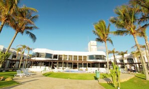 A modern hotel with a curved facade, a pool area, and palm trees.