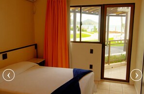A hotel room with a bed, a window with a view of a landscaped area, and a sliding door to an outdoor space.