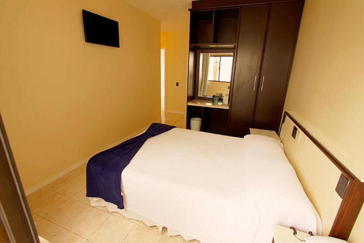 Un dormitorio con cama, armario, espejo y una ventana pequeña.