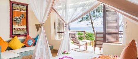 A bedroom with a bed, a canopy, a view of the sea, and a colorful wall tapestry.