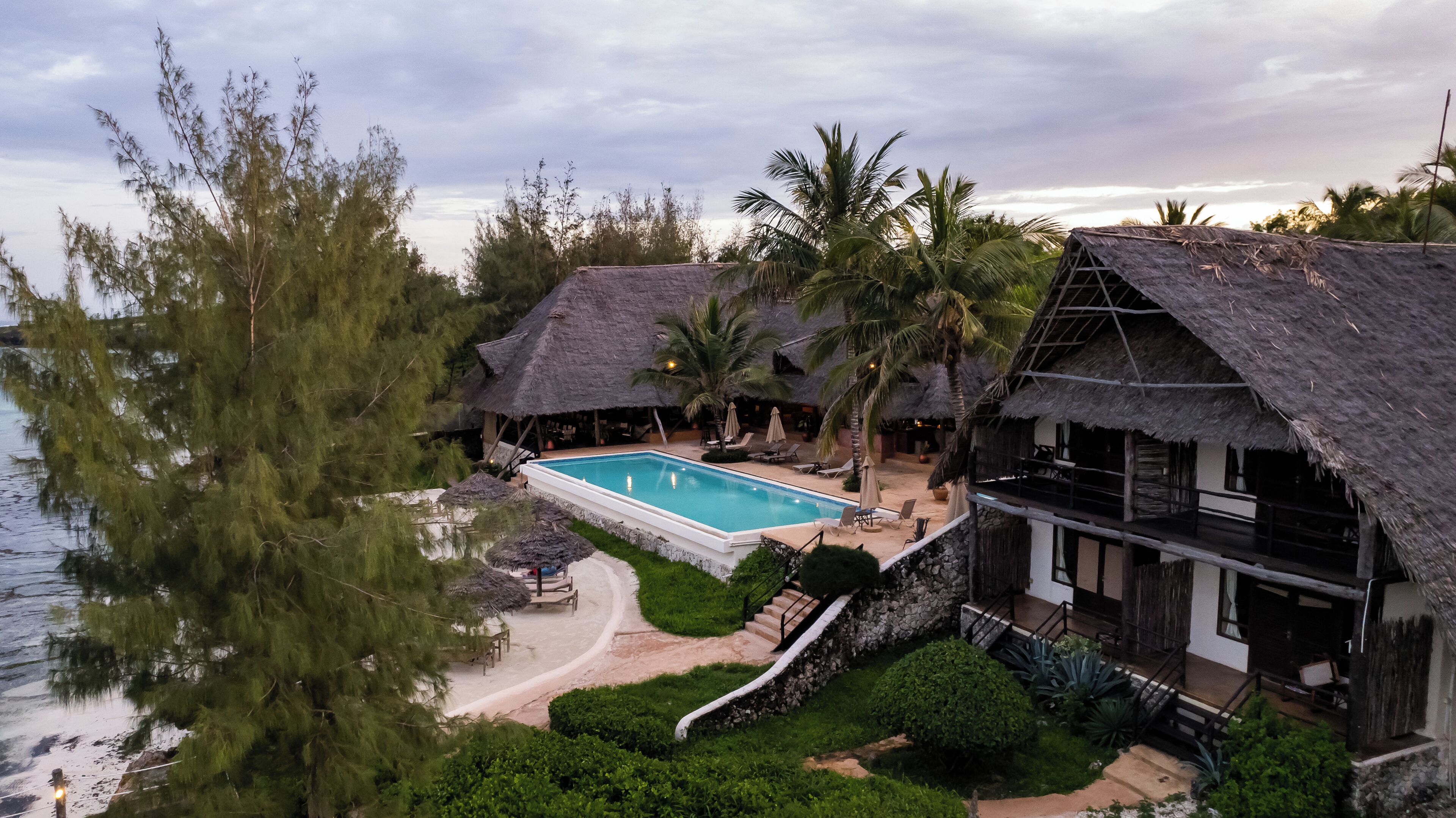 Un resort con piscina, estructuras de techo de paja y vista al mar.