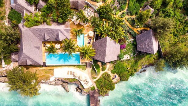 An aerial view of a resort with a swimming pool, palm trees, and a dock by the sea. - Sunshine Marine Lodge (Matemwe)