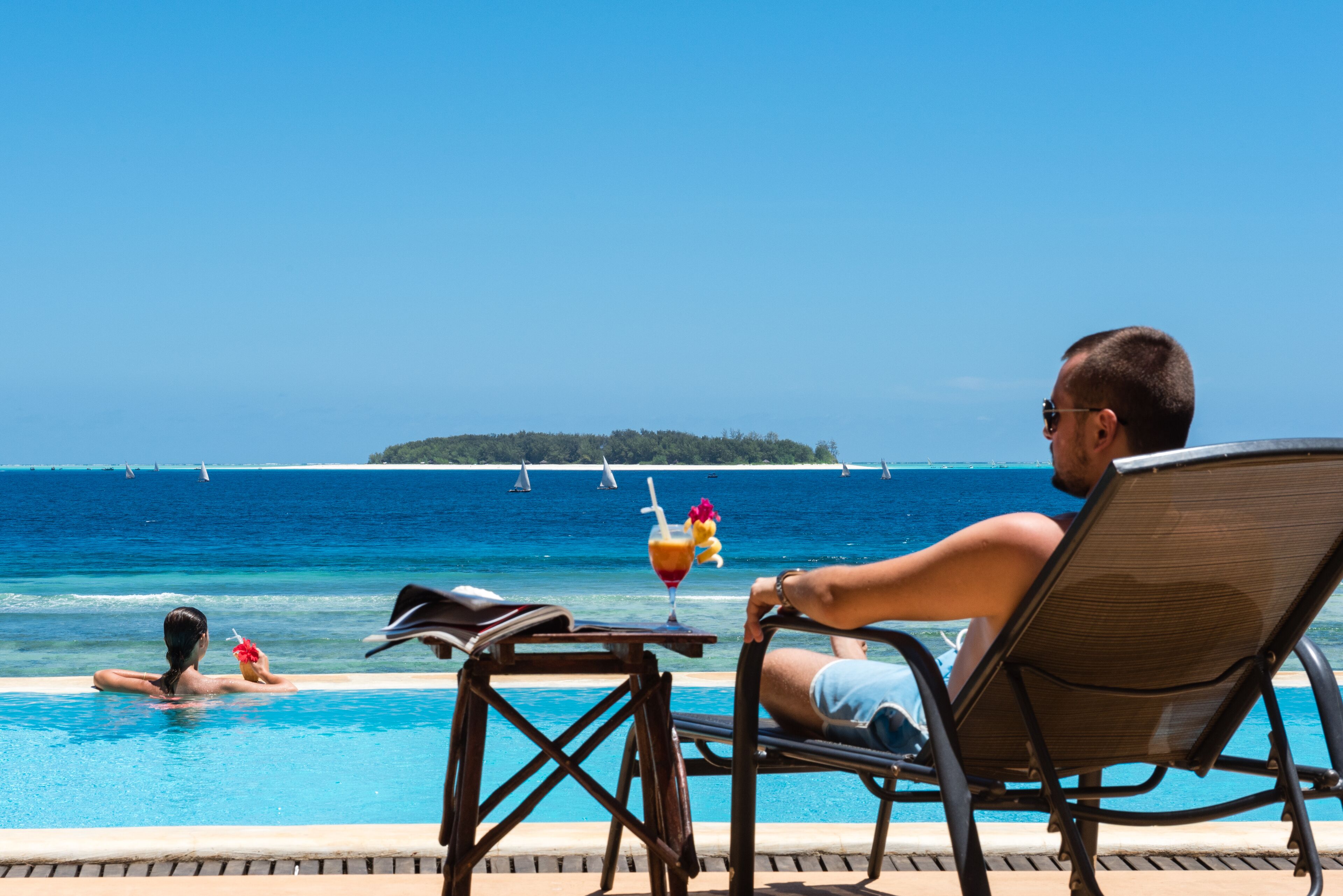 A poolside area with a lounge chair and a table with a drink.