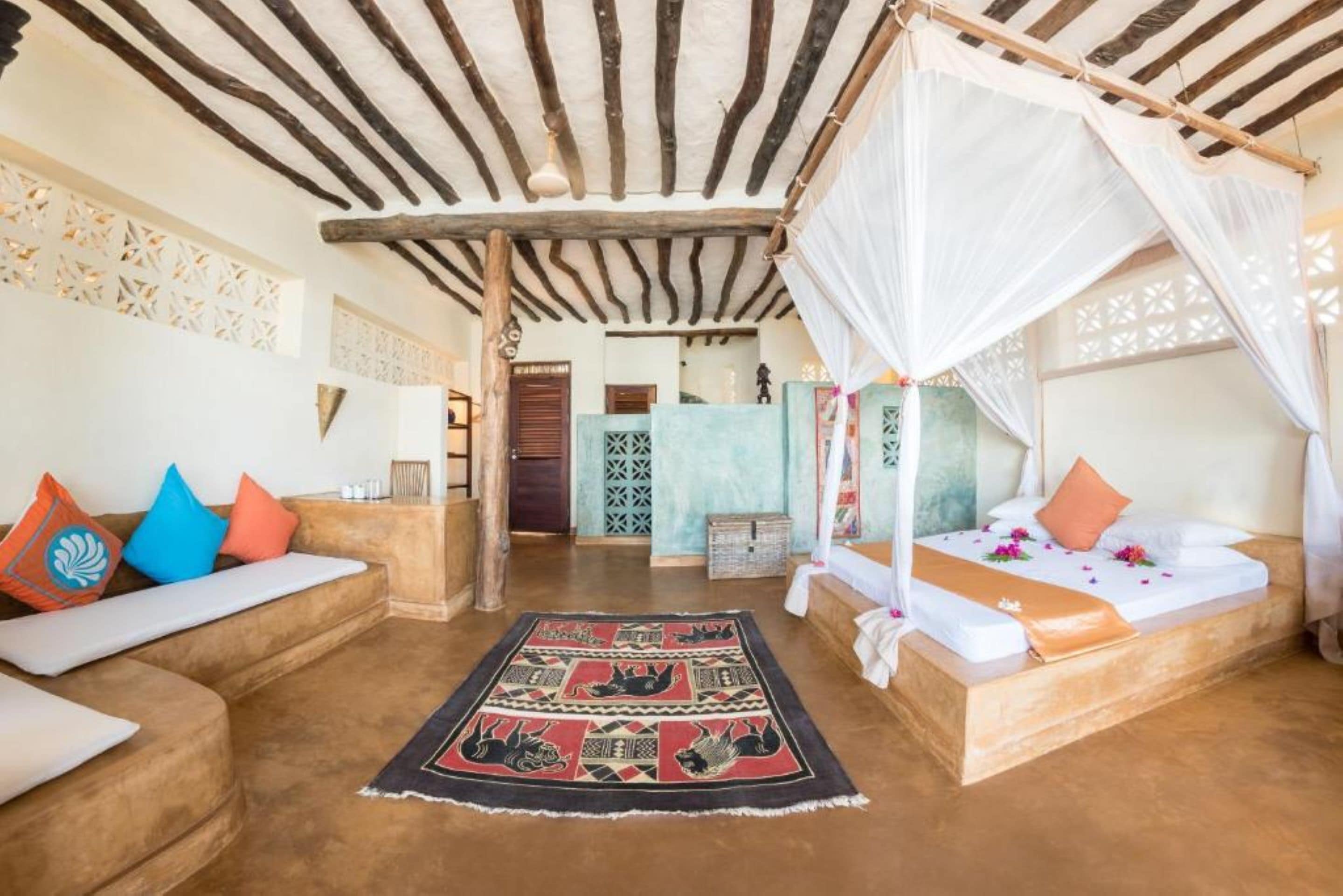 A room with a bed under a canopy, a sofa with cushions, a patterned rug, and a decorative wall.