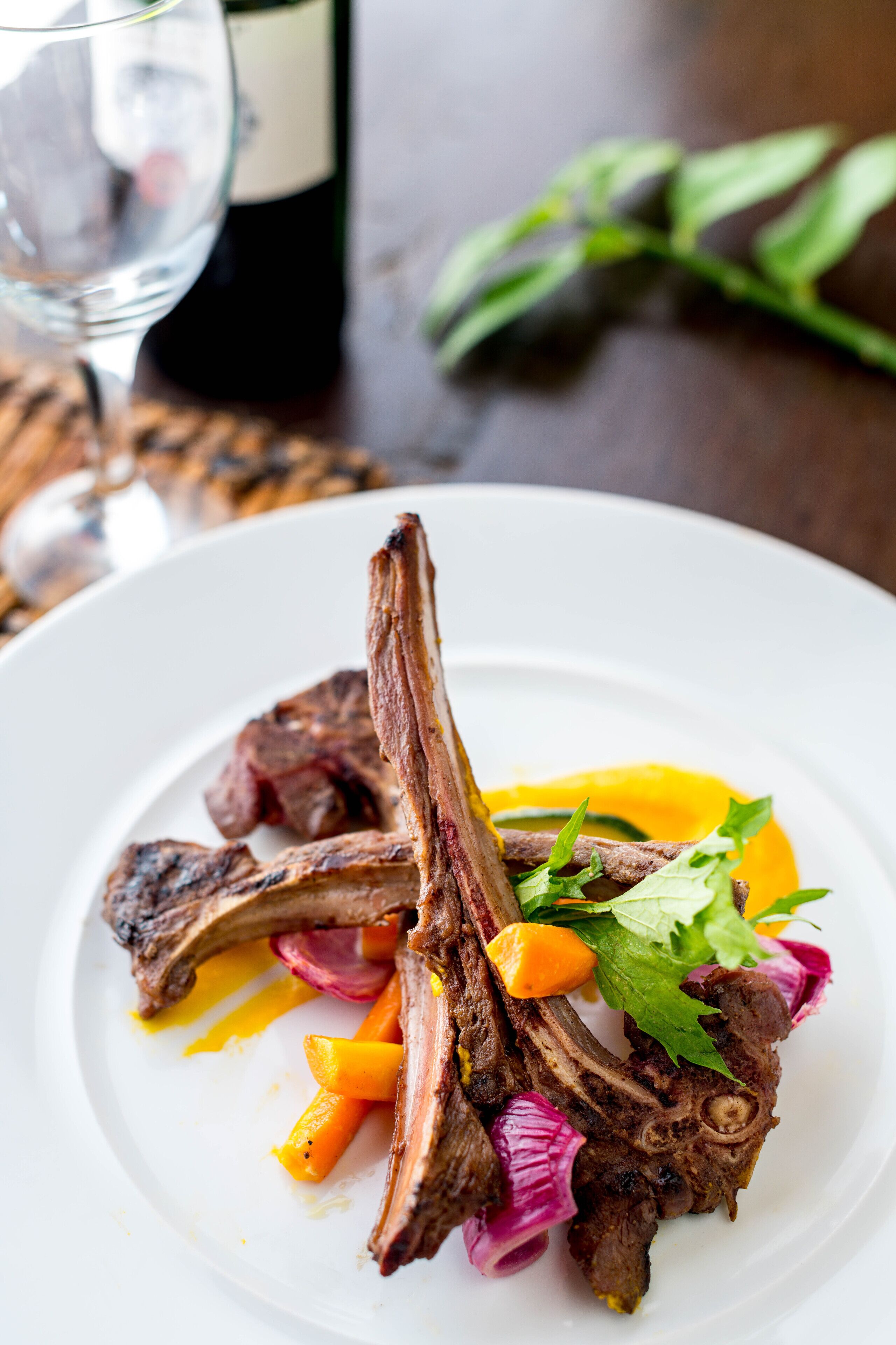 A plate of food with lamb chops, carrots, and a yellow sauce.