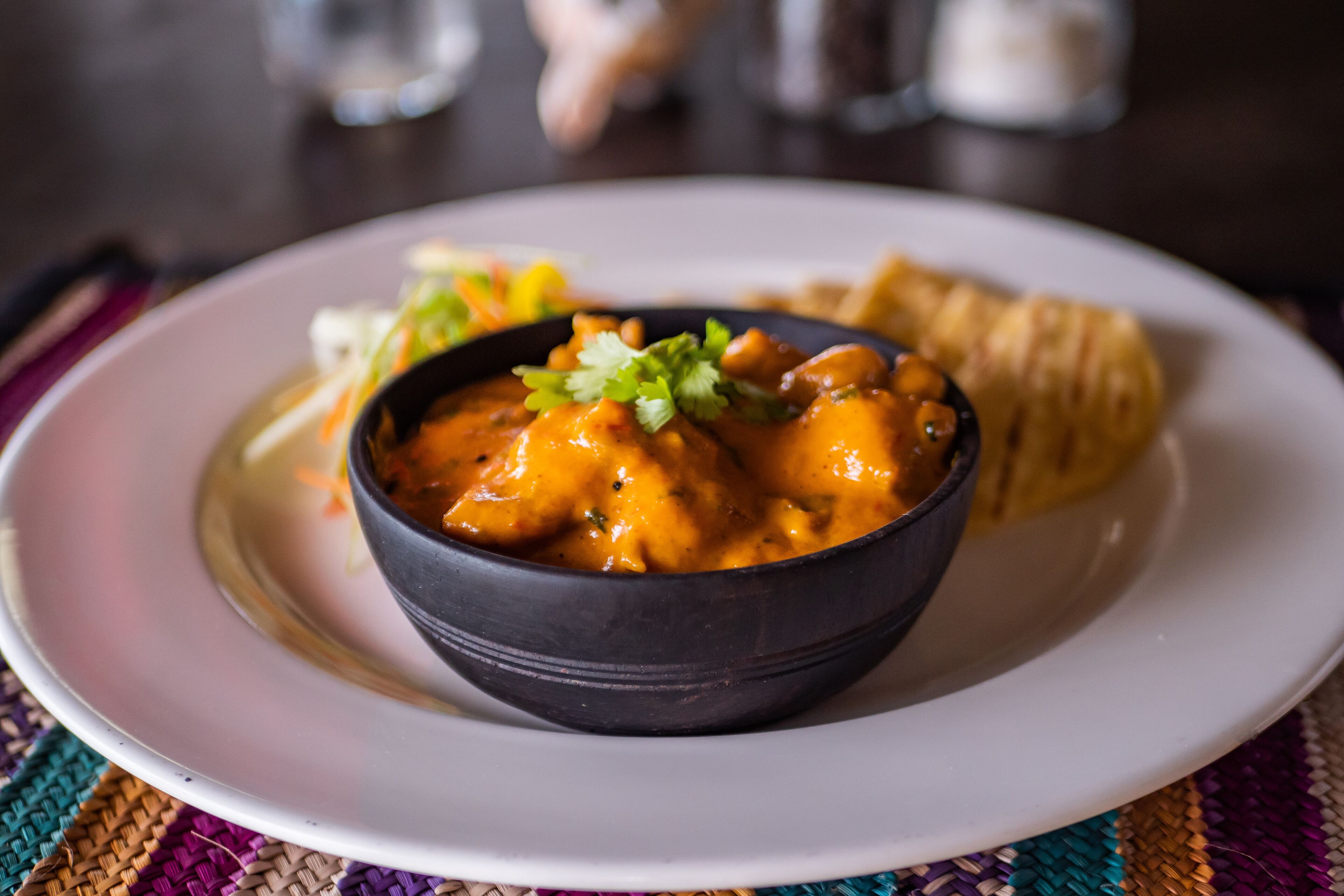A bowl of curry with naan bread on a white plate.