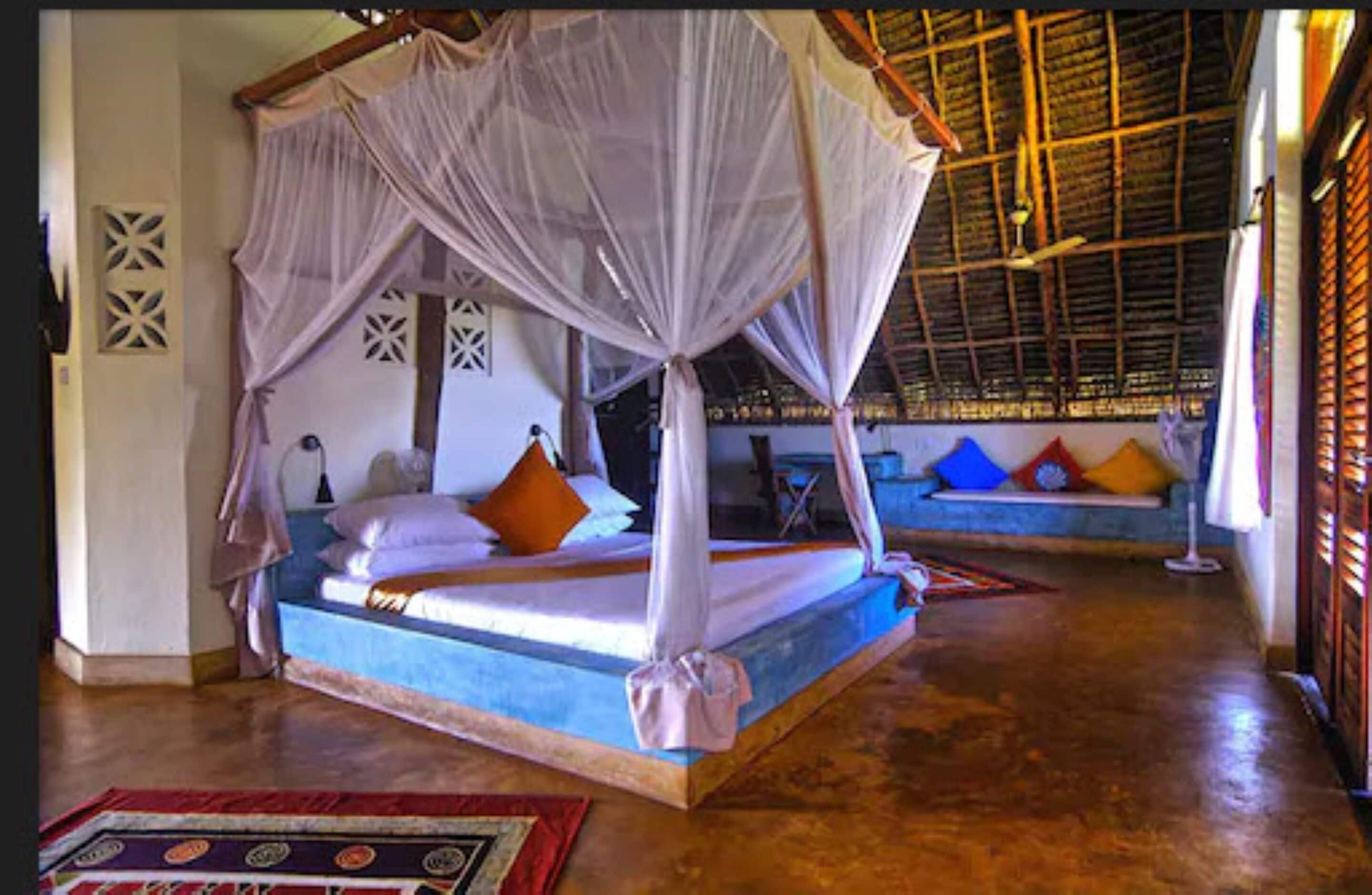 A room with a bed under a canopy, a sofa with cushions, and a wooden floor.