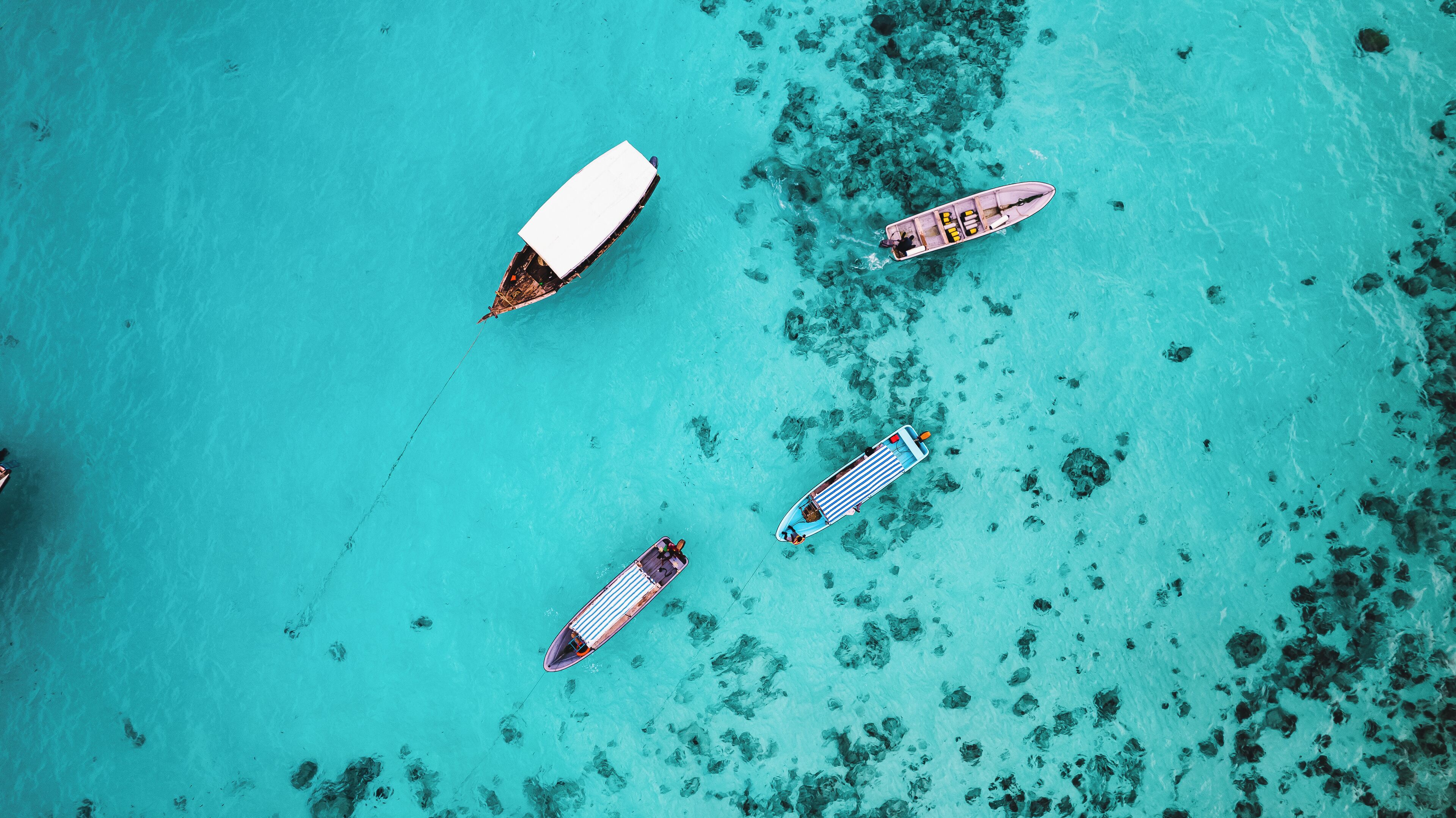 An aerial view of a turquoise lagoon with four boats anchored.