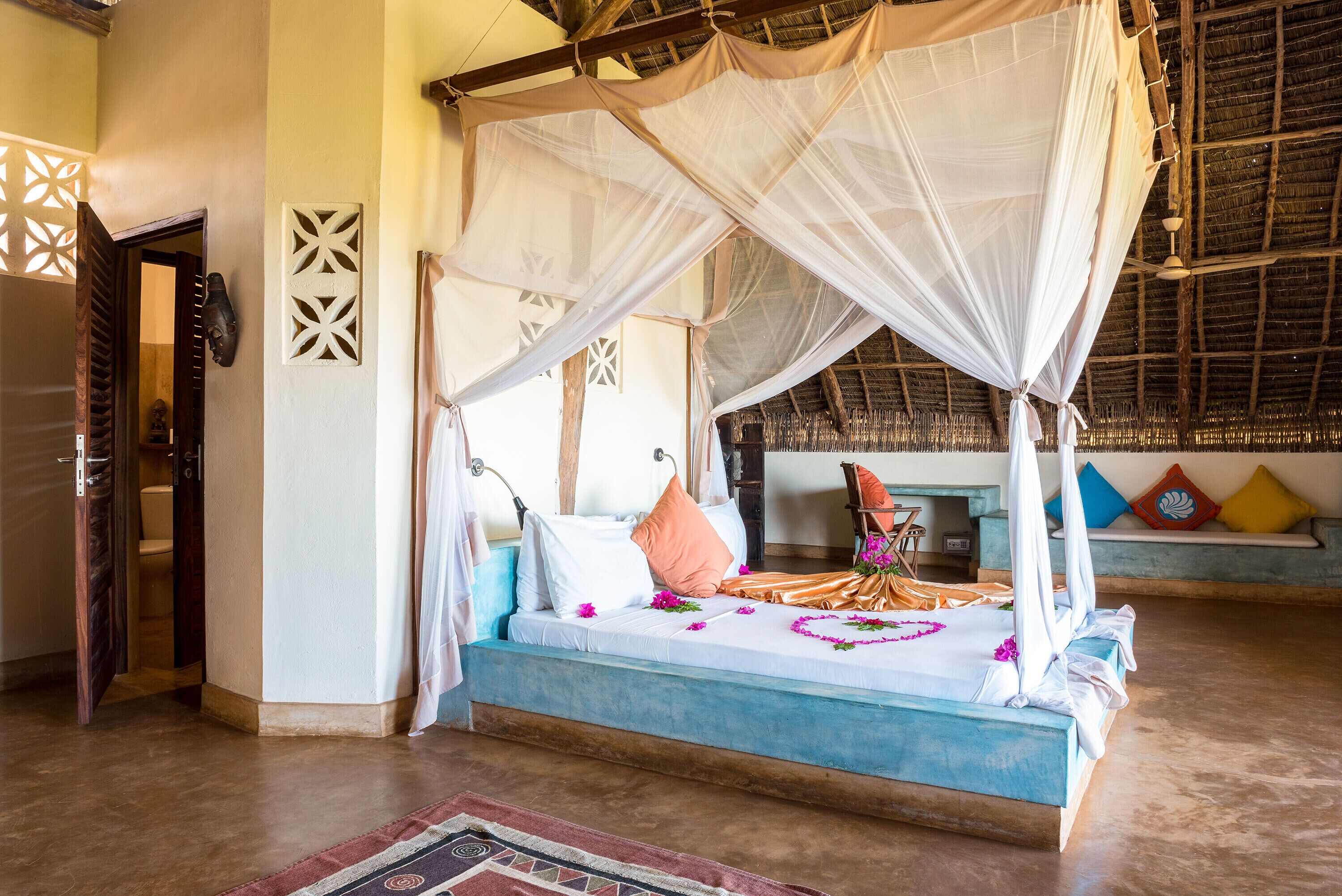 A four-poster bed with a canopy, a wooden bench, and a small table with a chair.