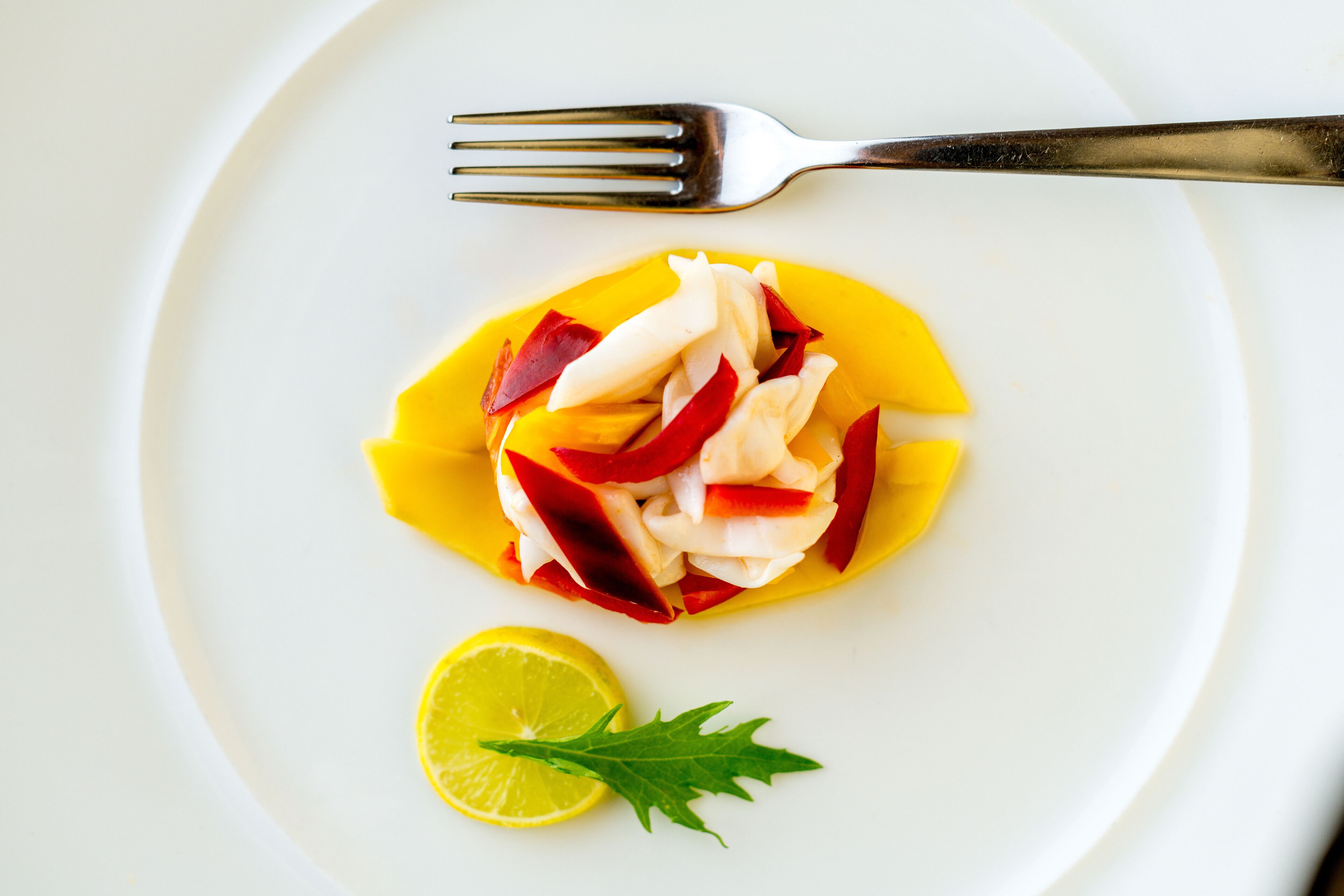 Une assiette blanche contenant un plat de poisson, une tranche de citron et une garniture.
