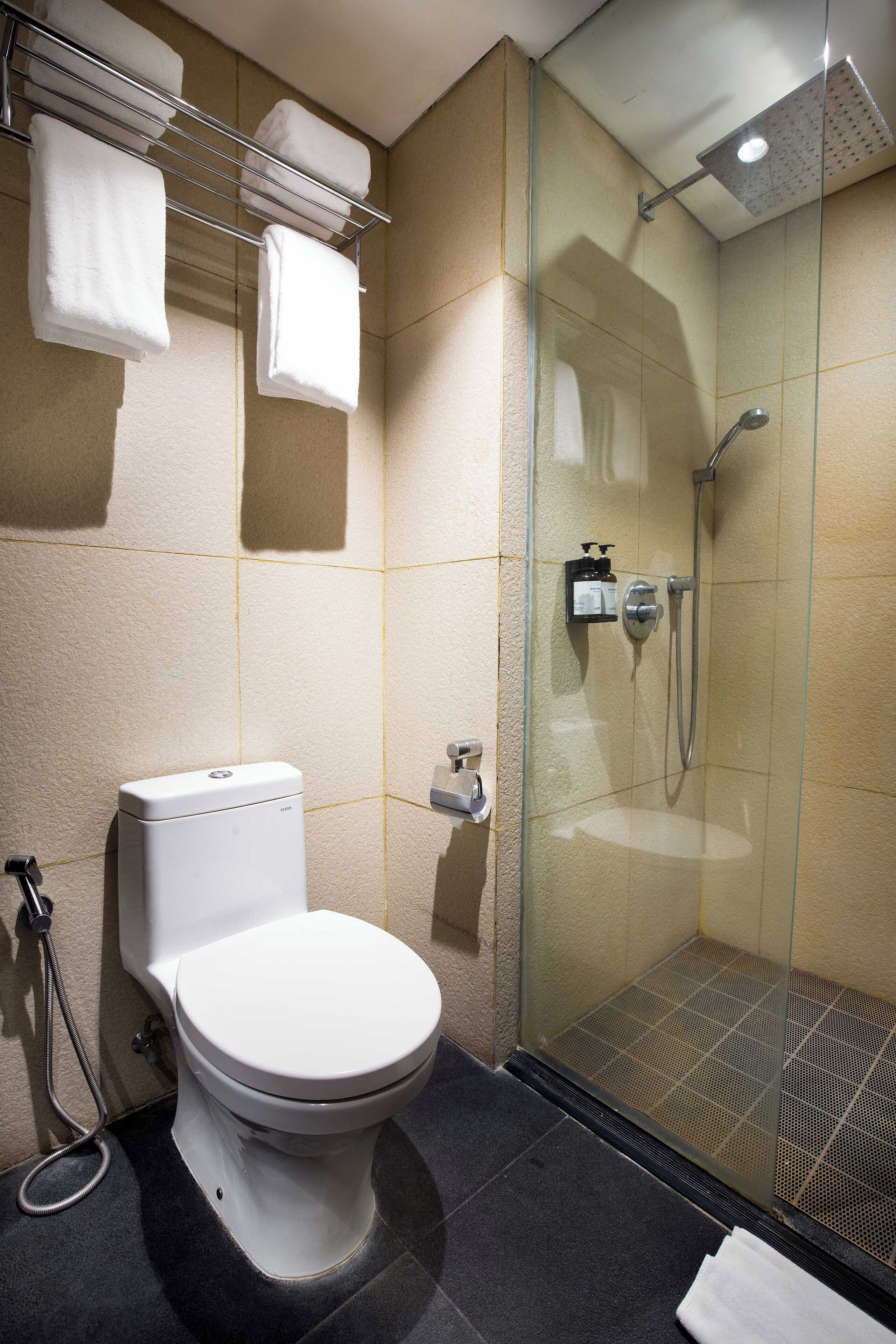 A modern bathroom with a toilet, glass shower enclosure, and a towel rack with towels.