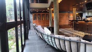 Un interior moderno con una zona de estar con largo banco, una cocina al fondo y ventanas amplias que ofrecen vistas al exterior.